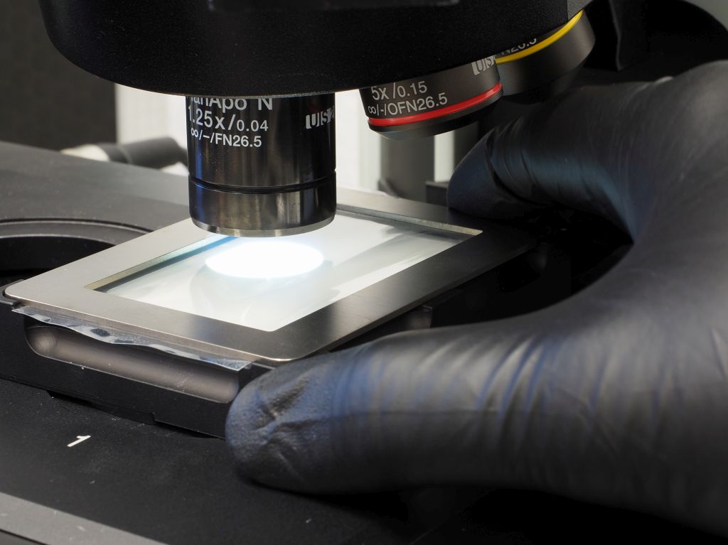 Figure 2: An operator places the holder containing the tape lift sample in the stage insert of the microscope system to prepare it for the cleanliness analysis